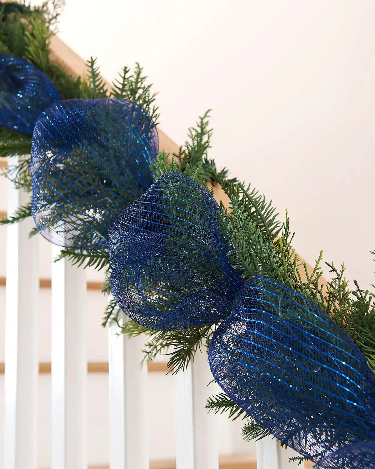 Garland on a staircase banister with blue mesh ribbon and greenery on a white background