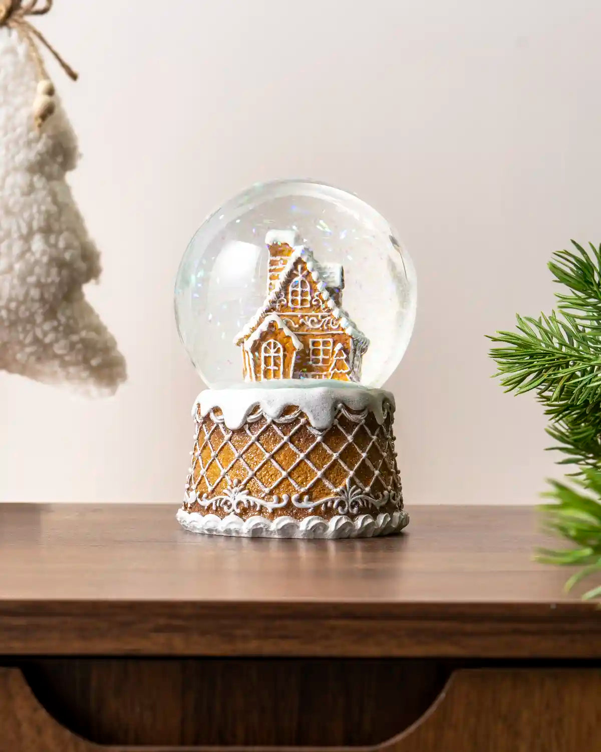 Gingerbread snow globe displayed on a wooden table, with a decorated gingerbread house inside a clear dome and lattice detailing on the base