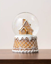 Gingerbread snow globe featuring a detailed gingerbread house inside a clear glass dome, decorated with white icing