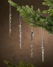 Glass icicle-shaped ornaments hanging from a Christmas tree branch against a brown background