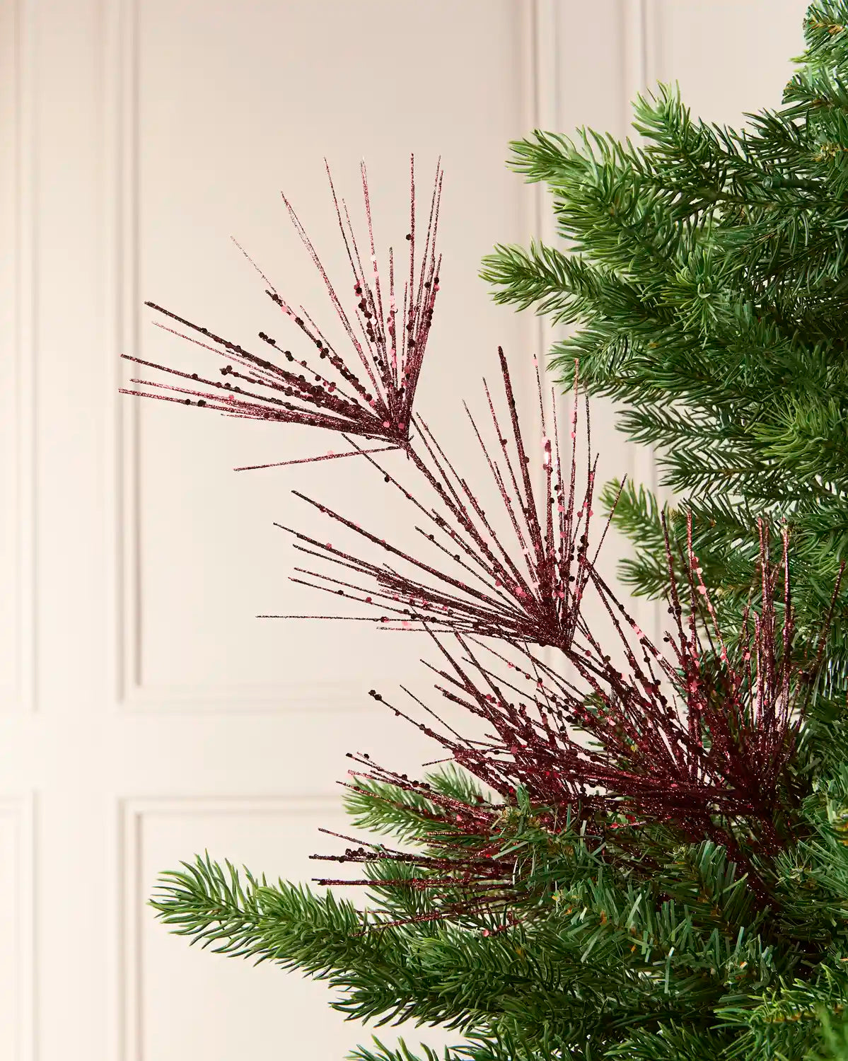 Glitter Firework Spray in  Burgundy , featuring multiple thin, glitter-covered branches in a firework shape against a green Christmas tree.
