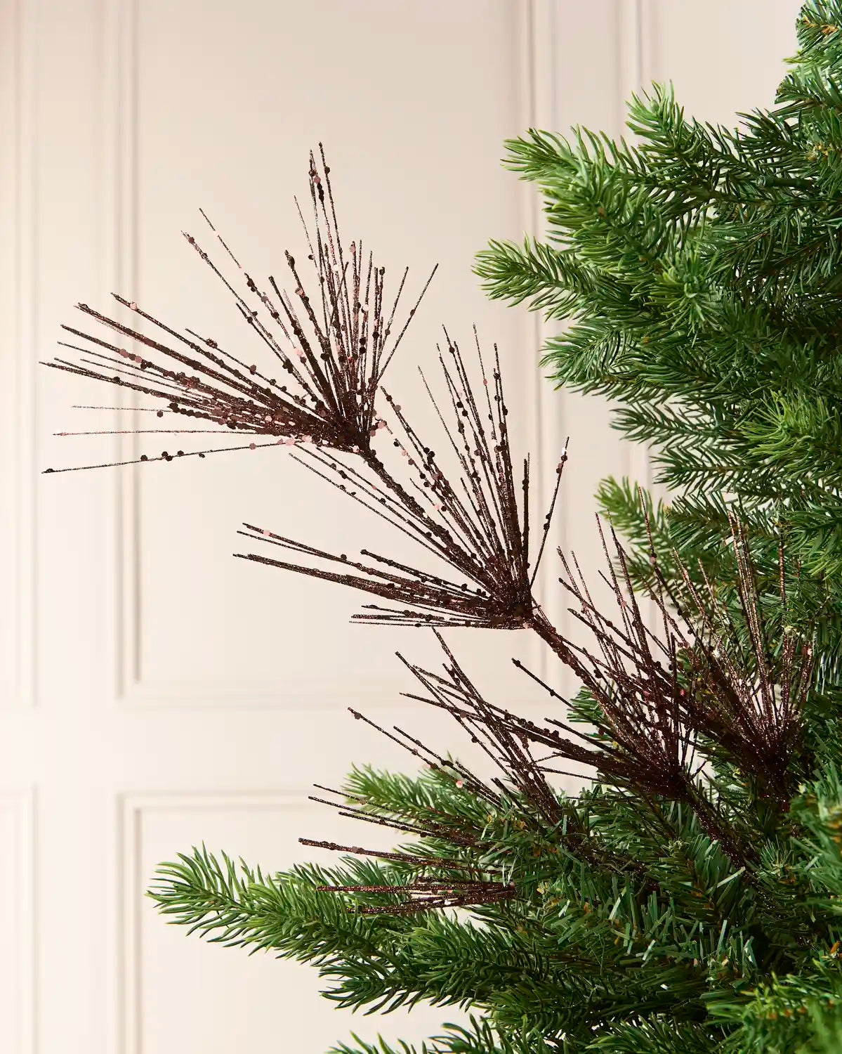 Glitter Firework Spray in  Espresso , featuring multiple thin, glitter-covered branches in a firework shape against a green Christmas tree.
