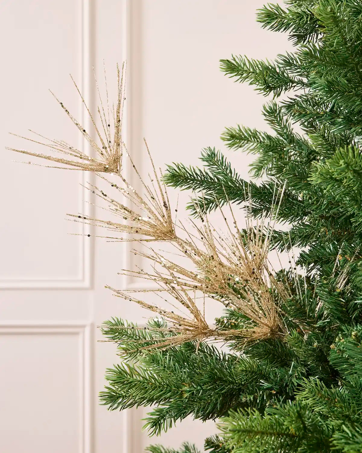 Glitter Firework Spray in Latte, featuring multiple thin, glitter-covered branches in a firework shape against a green Christmas tree.
