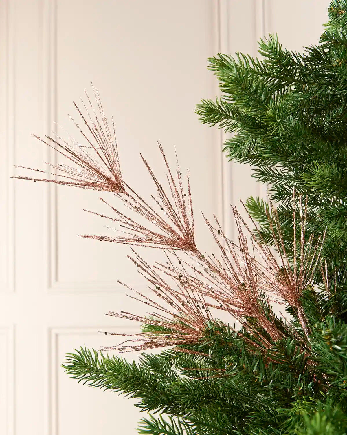 Glitter Firework Spray in  Rose Gold , featuring multiple thin, glitter-covered branches in a firework shape against a green Christmas tree.
