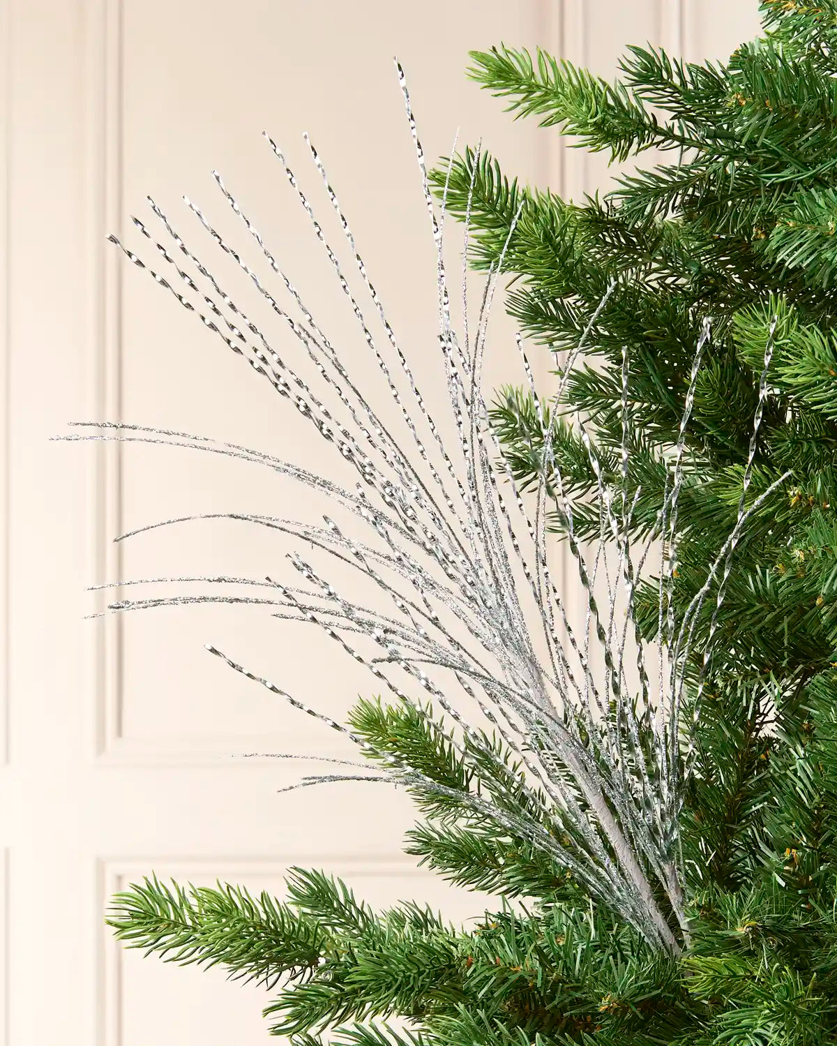 Glitter Fountain Christmas Tree Spray in Silver, featuring numerous shimmering, twisted sprays fanning outward among green Christmas tree branches
