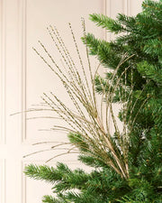 Glitter Fountain Christmas Tree Spray in gold, featuring numerous shimmering, twisted sprays fanning outward among green Christmas tree branches
