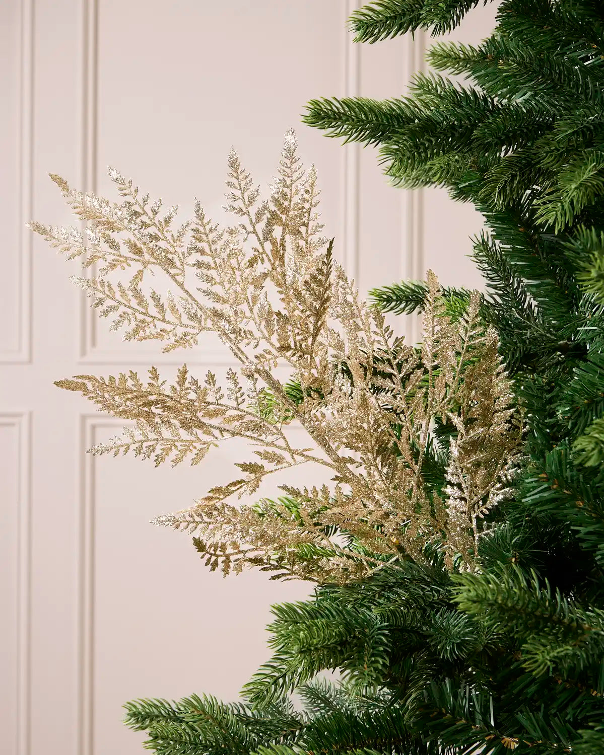 Glitter Leaf Christmas Tree Spray in gold placed in Christmas tree branches with  a cream paneled background