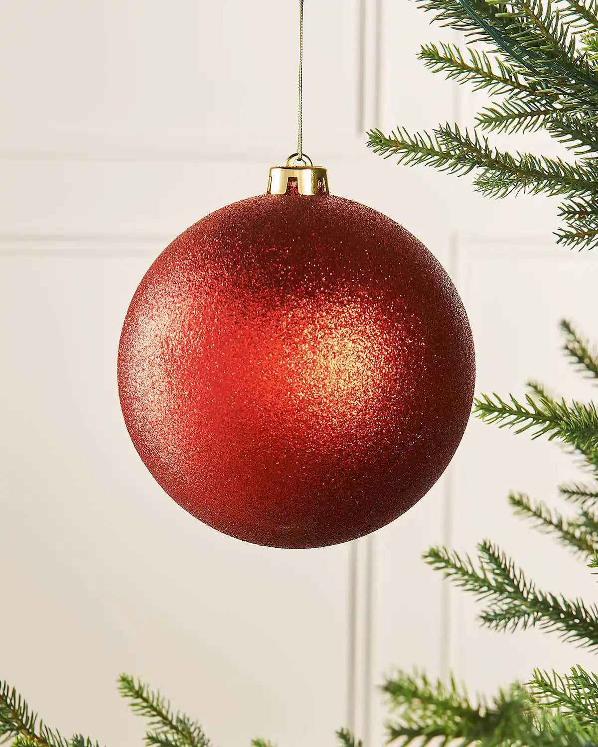 Glitter red oversized 15cm bauble on a Christmas tree branch