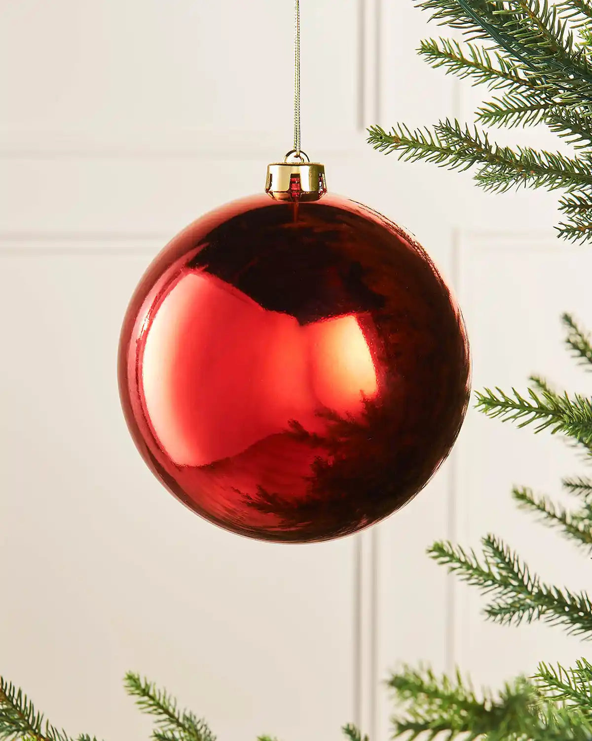 Gloss 15cm oversized bauble on a Christmas tree branch against a cream panel background