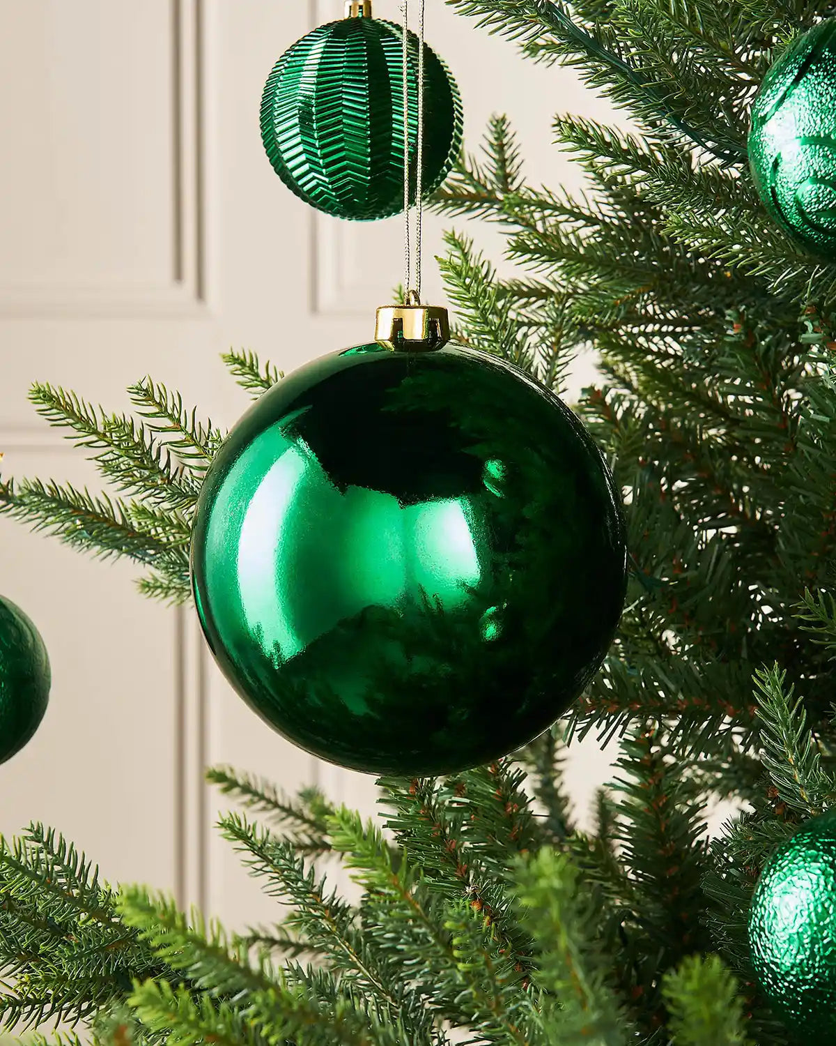 Gloss Christmas green 15cm oversized bauble on a Christmas tree branch with 4 smaller green baubles in background
