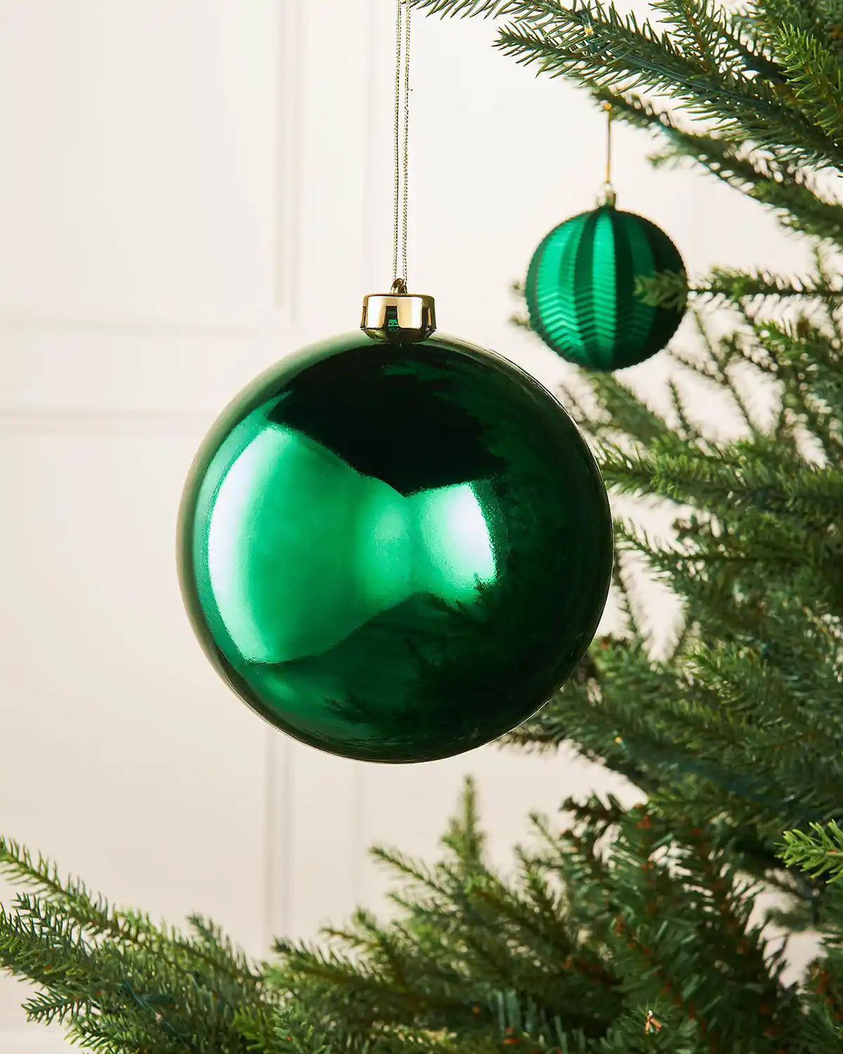 Gloss Christmas green 15cm oversized bauble on a Christmas tree branch with a smaller green bauble in background