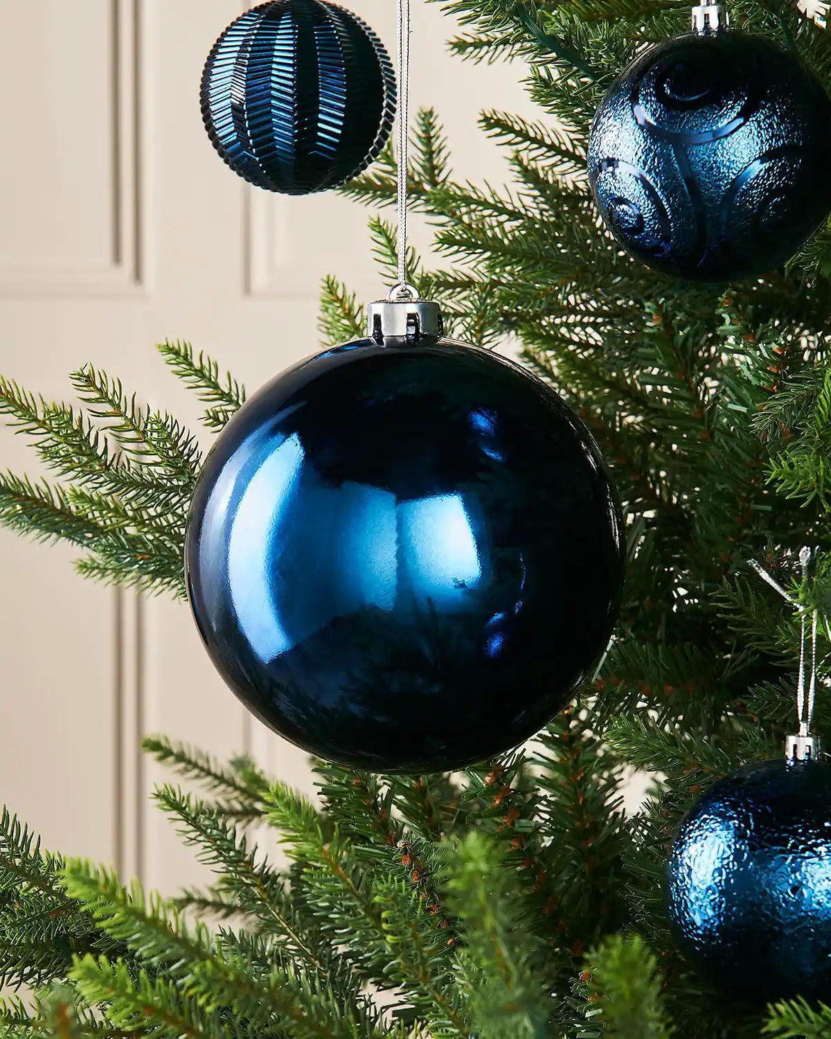 Gloss Navy blue 15cm oversized bauble on a Christmas tree branch with 4 smaller blue baubles in background