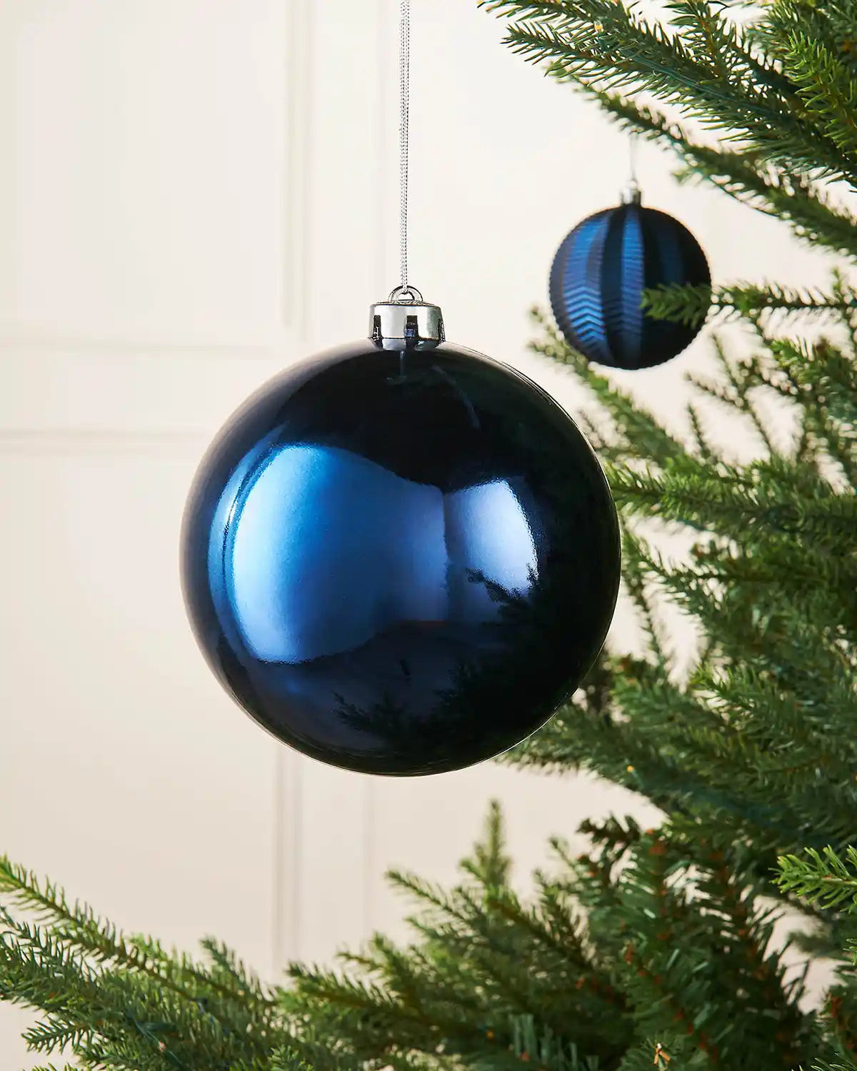 Gloss Navy blue 15cm oversized bauble on a Christmas tree branch with a smaller blue bauble in background