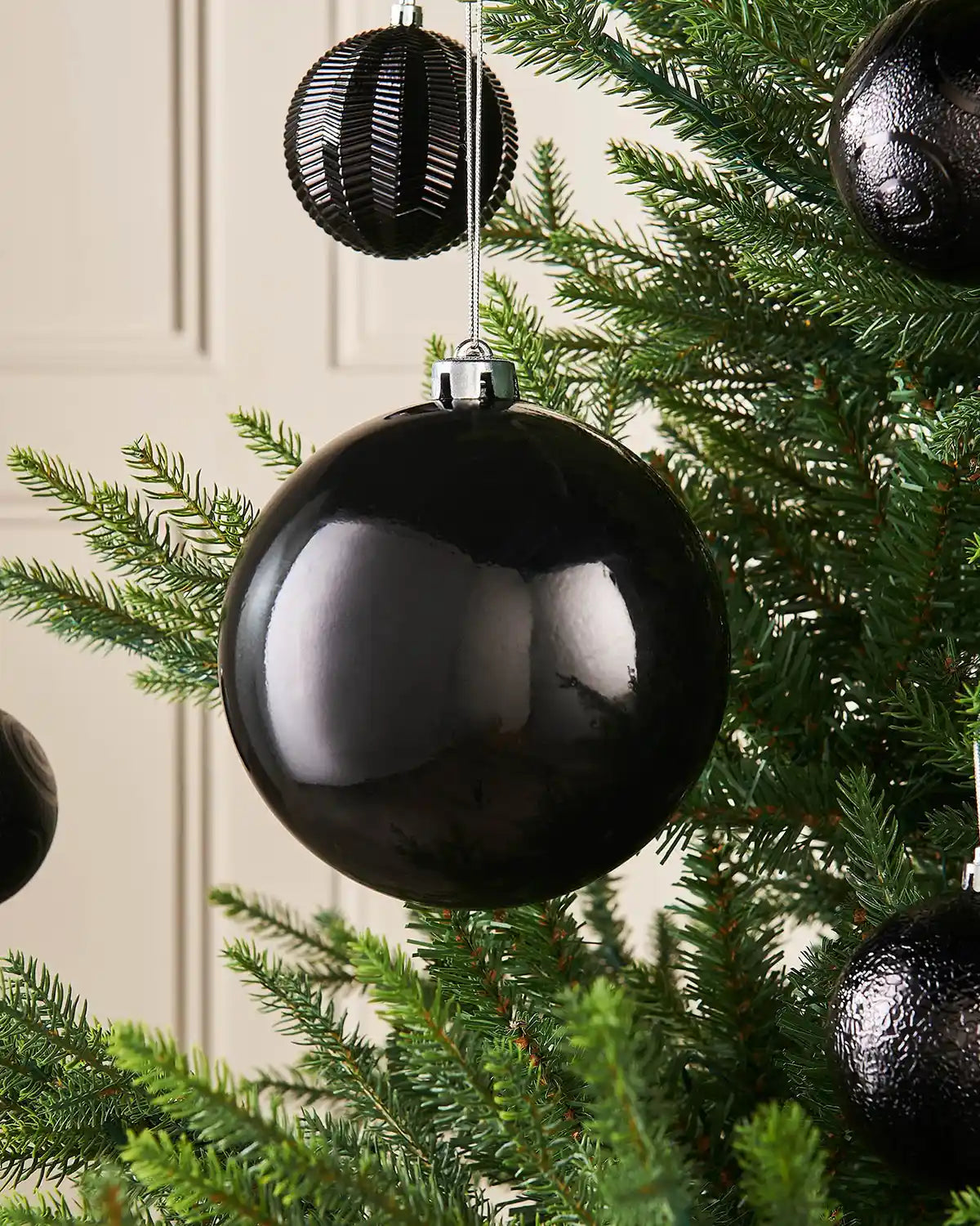 Gloss black oversized 15cm bauble on a Christmas tree branch with 4 smaller black baubles in background