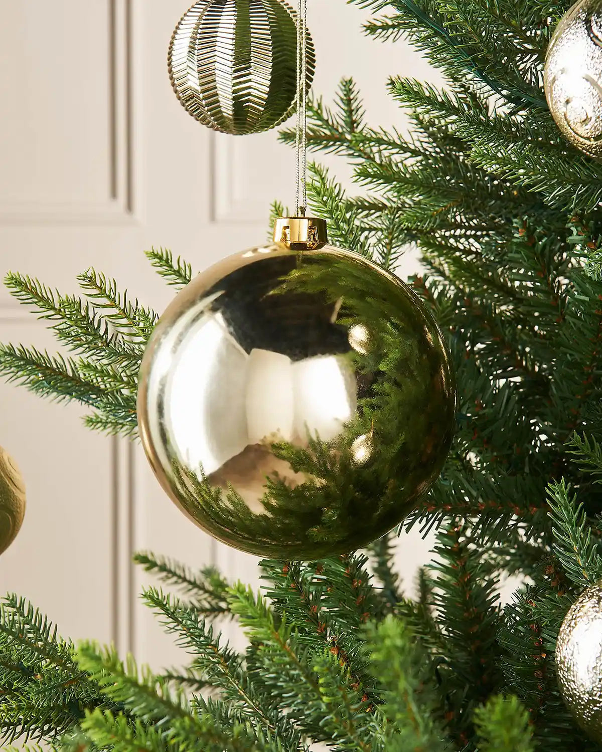 Gloss gold 15m oversized bauble on a Christmas tree branch with 4 smaller gold baubles in the background
