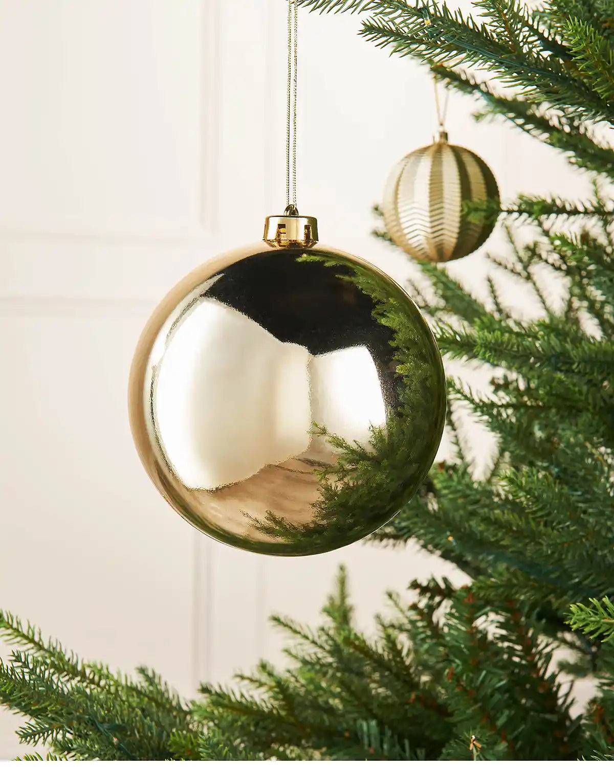 Gloss gold 15m oversized bauble on a Christmas tree branch with a smaller gold bauble in the background