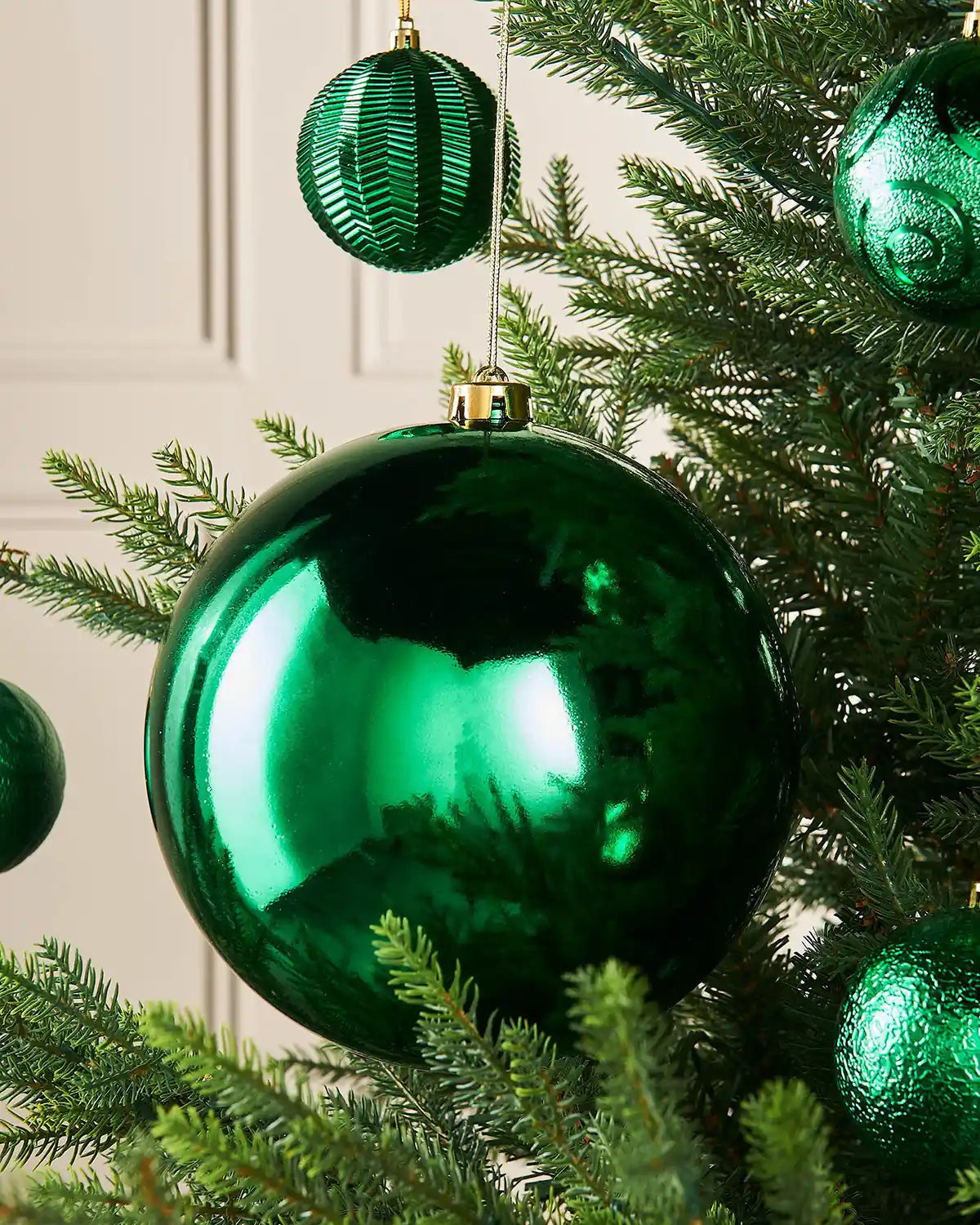 Gloss green oversized bauble on a Christmas tree branch with 4 smaller green baubles in the background