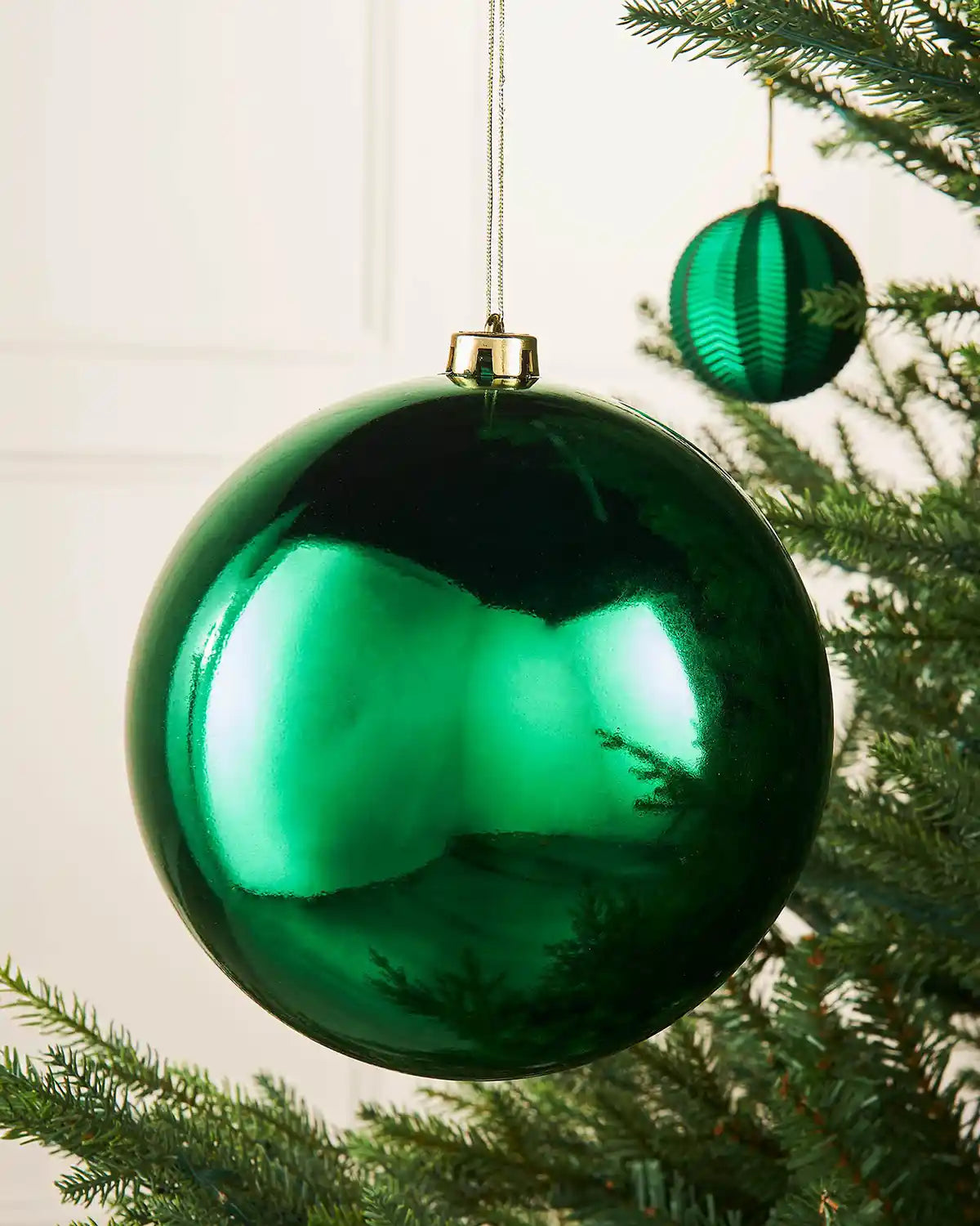 Gloss green oversized bauble on a Christmas tree branch with a smaller green bauble in the background