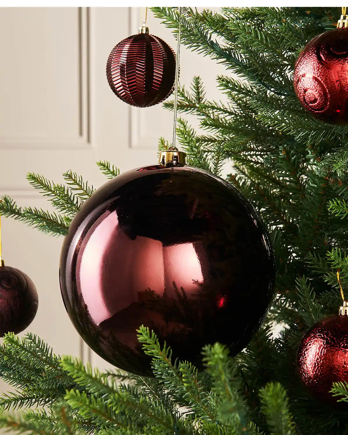 Gloss oversized burgundy bauble on a Christmas tree branch with 4 smaller burgundy baubles in the background