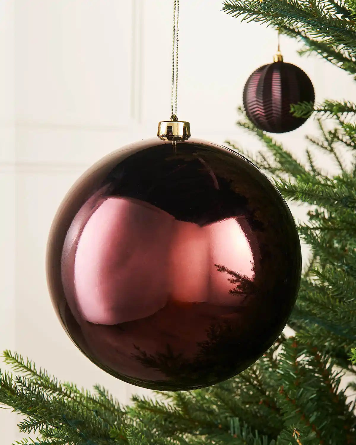 Gloss oversized burgundy bauble on a Christmas tree branch with a smaller burgundy bauble in the background