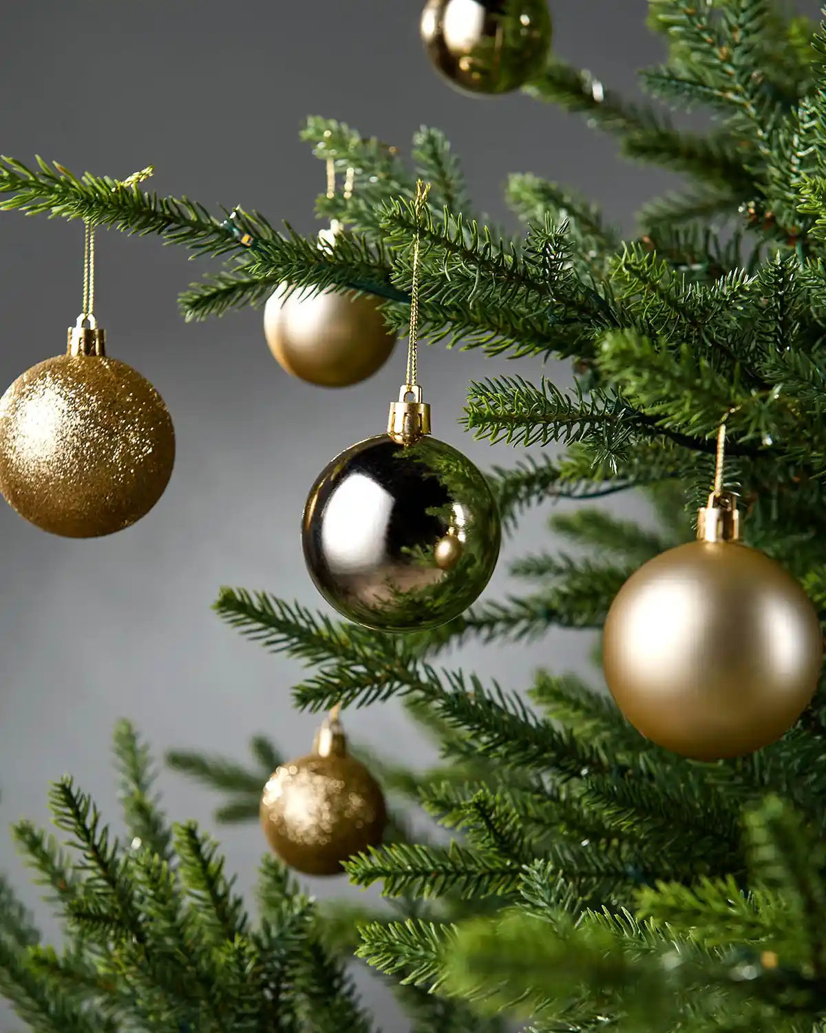 Gold Christmas baubles on a tree with a grey background