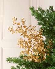 Gold Foliage Spray arranged among green Christmas Tree branches, showcasing its metallic gold leaves and delicate stems.