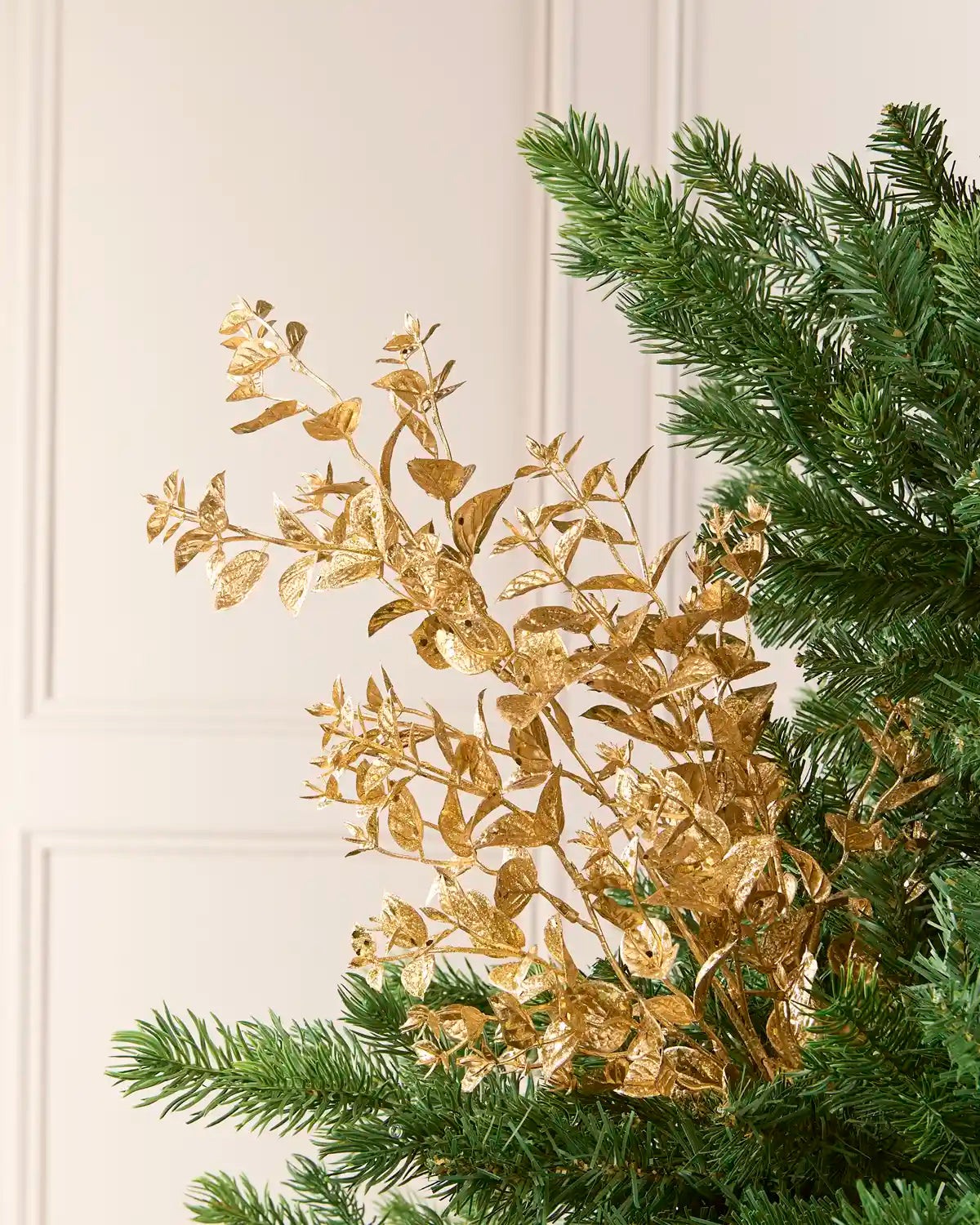 Gold Foliage Spray arranged among green Christmas Tree branches, showcasing its metallic gold leaves and delicate stems.