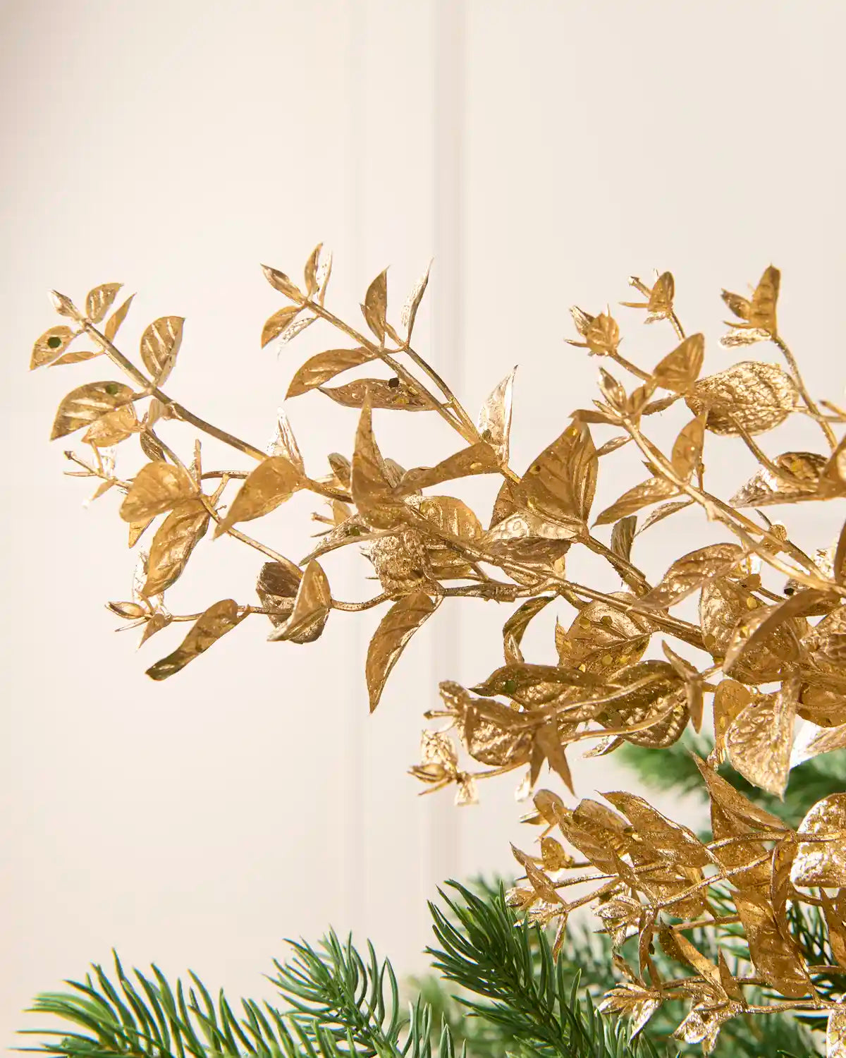 Gold Foliage Spray displayed among Christmas Tree branches, highlighting its layered gold leaves and decorative stems.