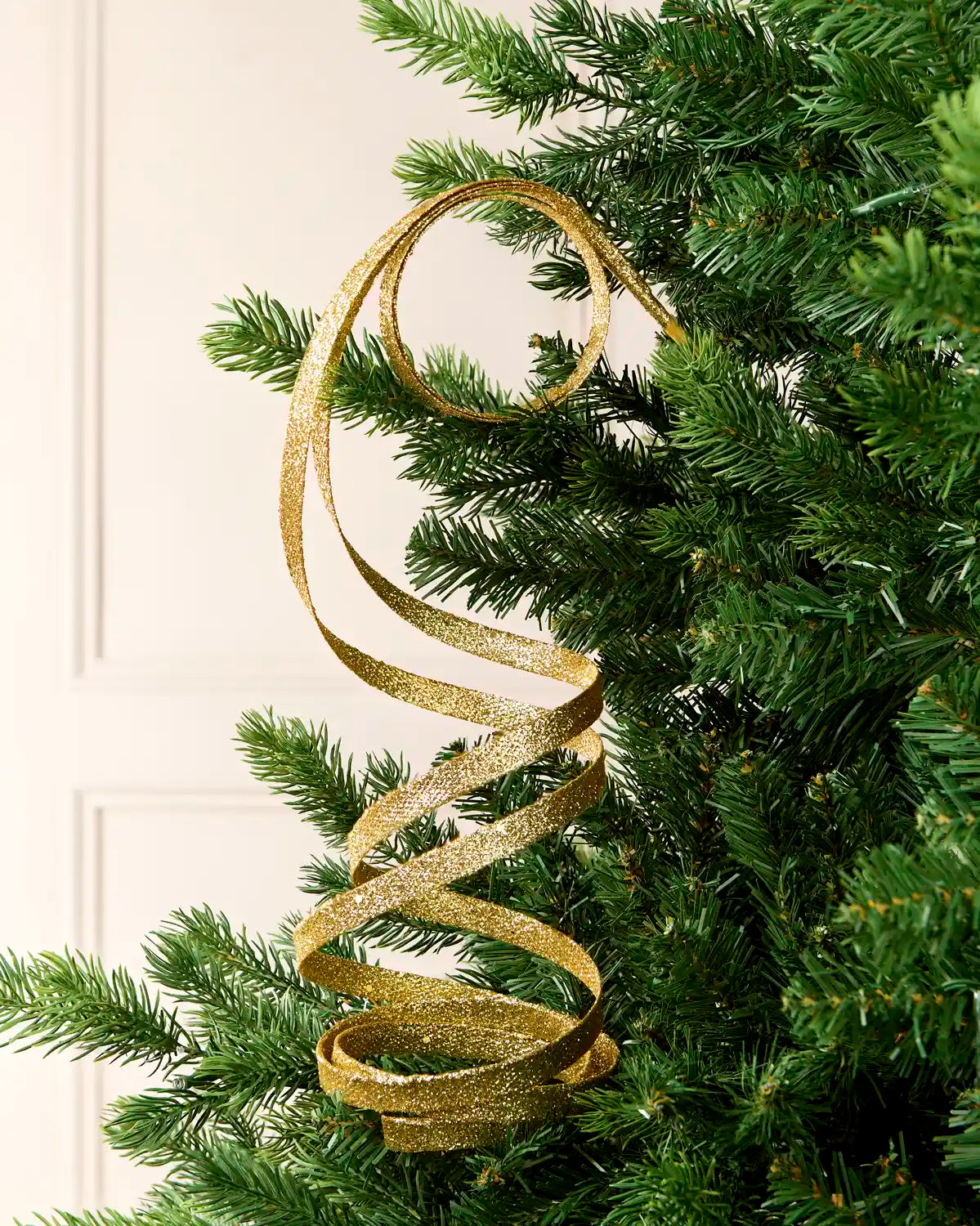 Gold Glitter Spiral Swirl Pick hanging from Christmas tree branch with cream background
