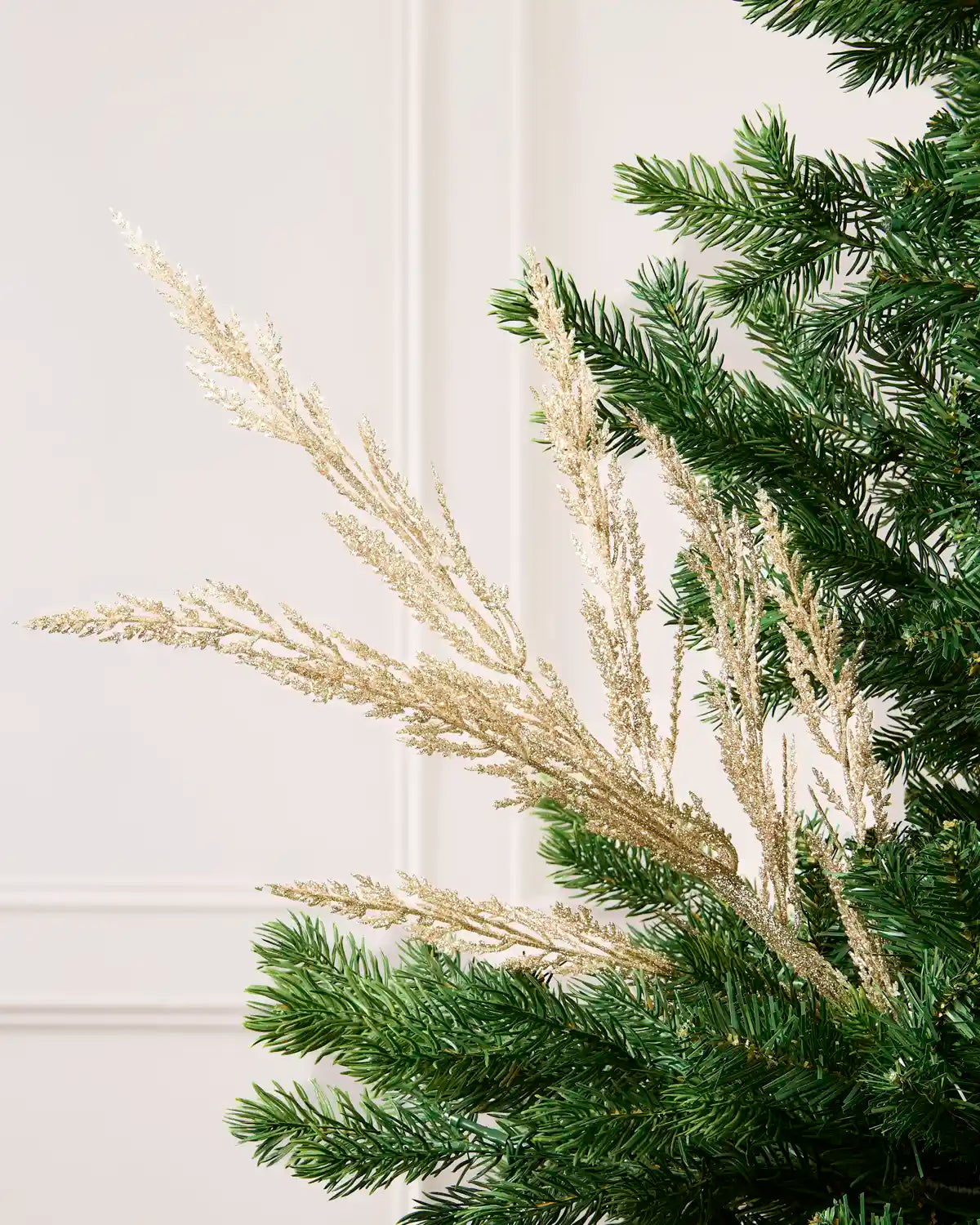 Gold Glitter Tip Christmas Tree Spray arranged in Christmas tree branches with a blurry cream background