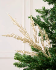Gold Glitter Tip Christmas Tree Spray arranged in Christmas tree branches with a blurry cream background