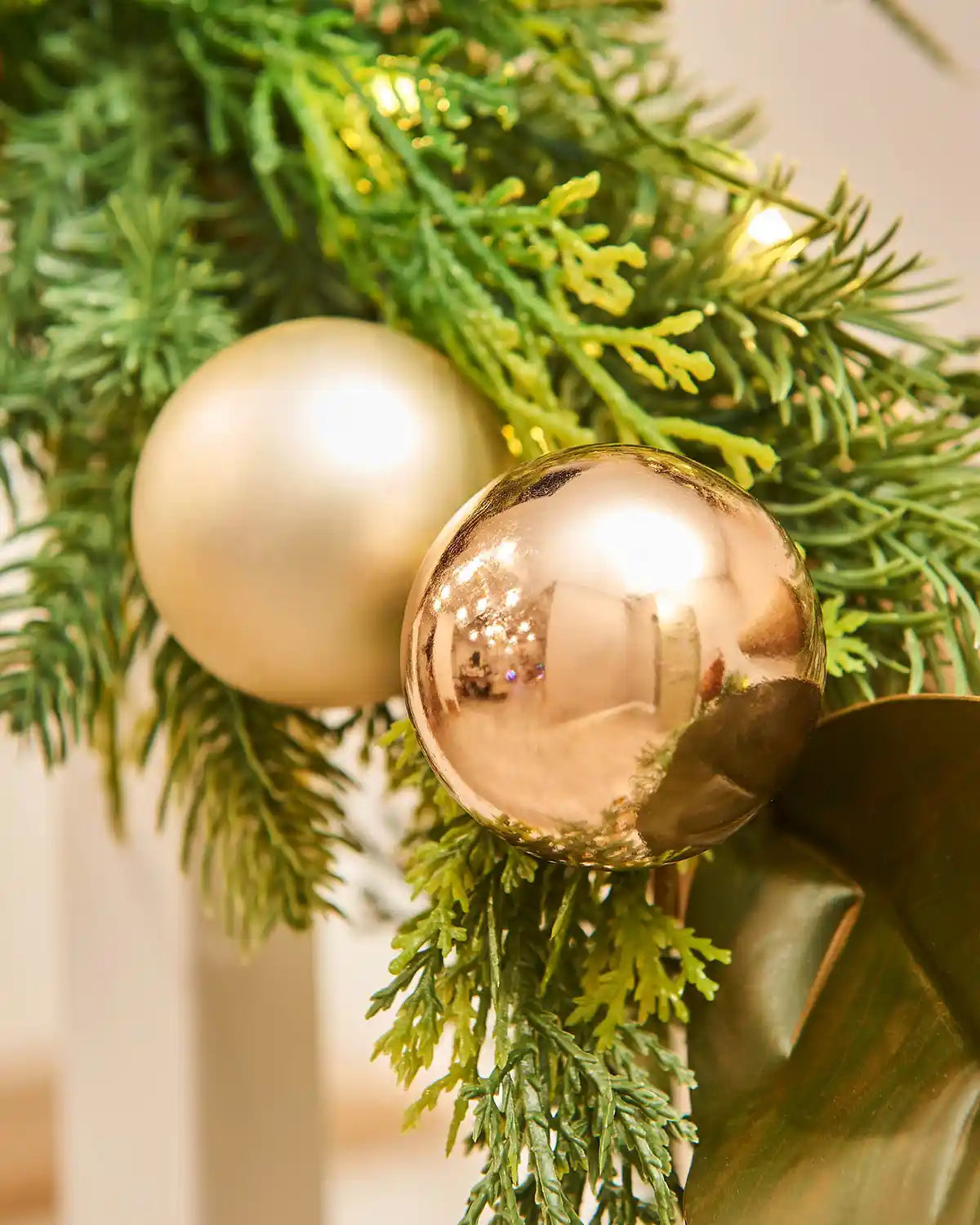 Gold and rose gold Christmas ornaments on green garland wrapped around wooden staircase banister 