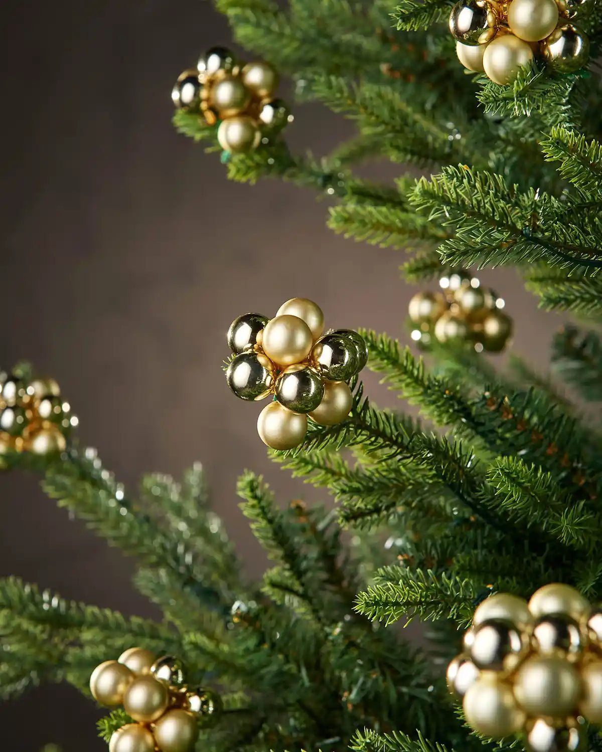 Gold berry cluster baubles on a Christmas tree with brown background