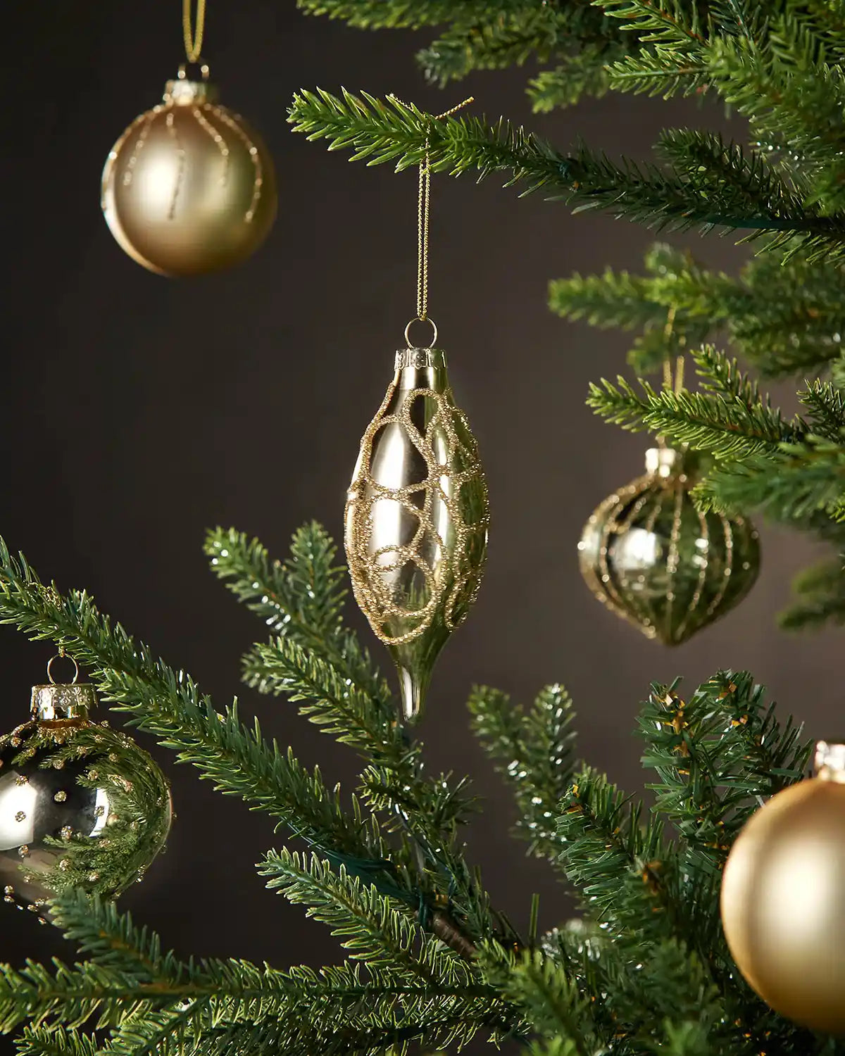 Gold glass Christmas baubles on a tree with a dark background