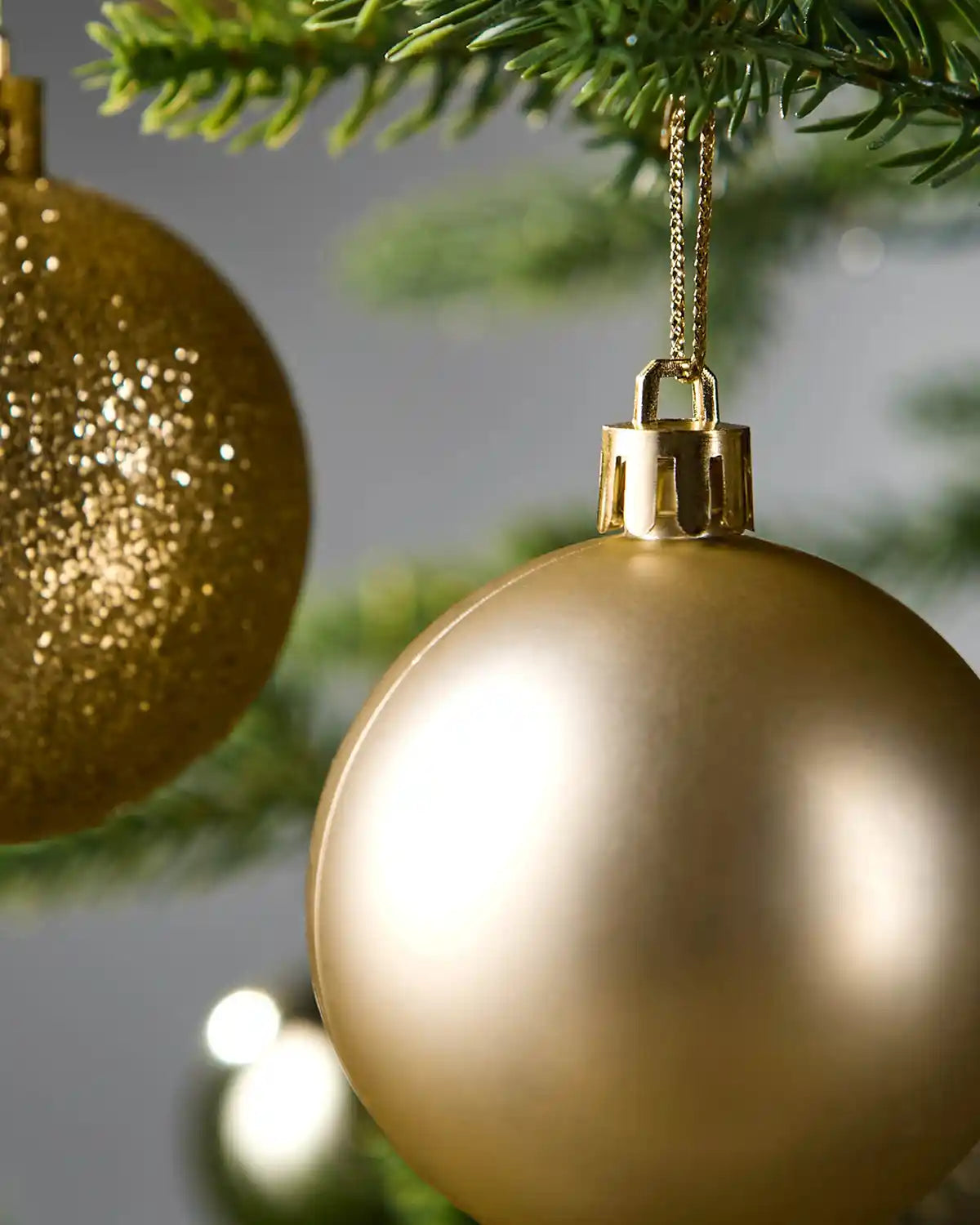 Gold glitter and matt Christmas baubles hanging on a tree branch with a blurred background