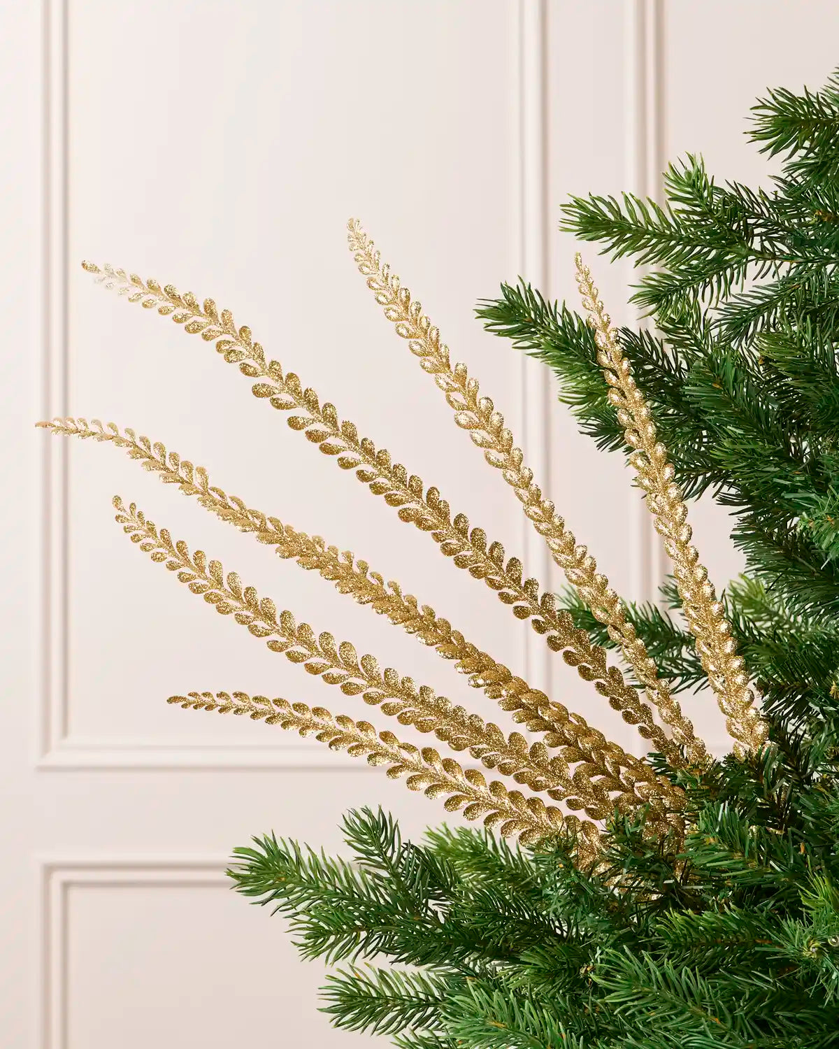 Gold glitter leaf spray with multiple glitter covered branches displayed against a cream background and green Christmas tree foliage