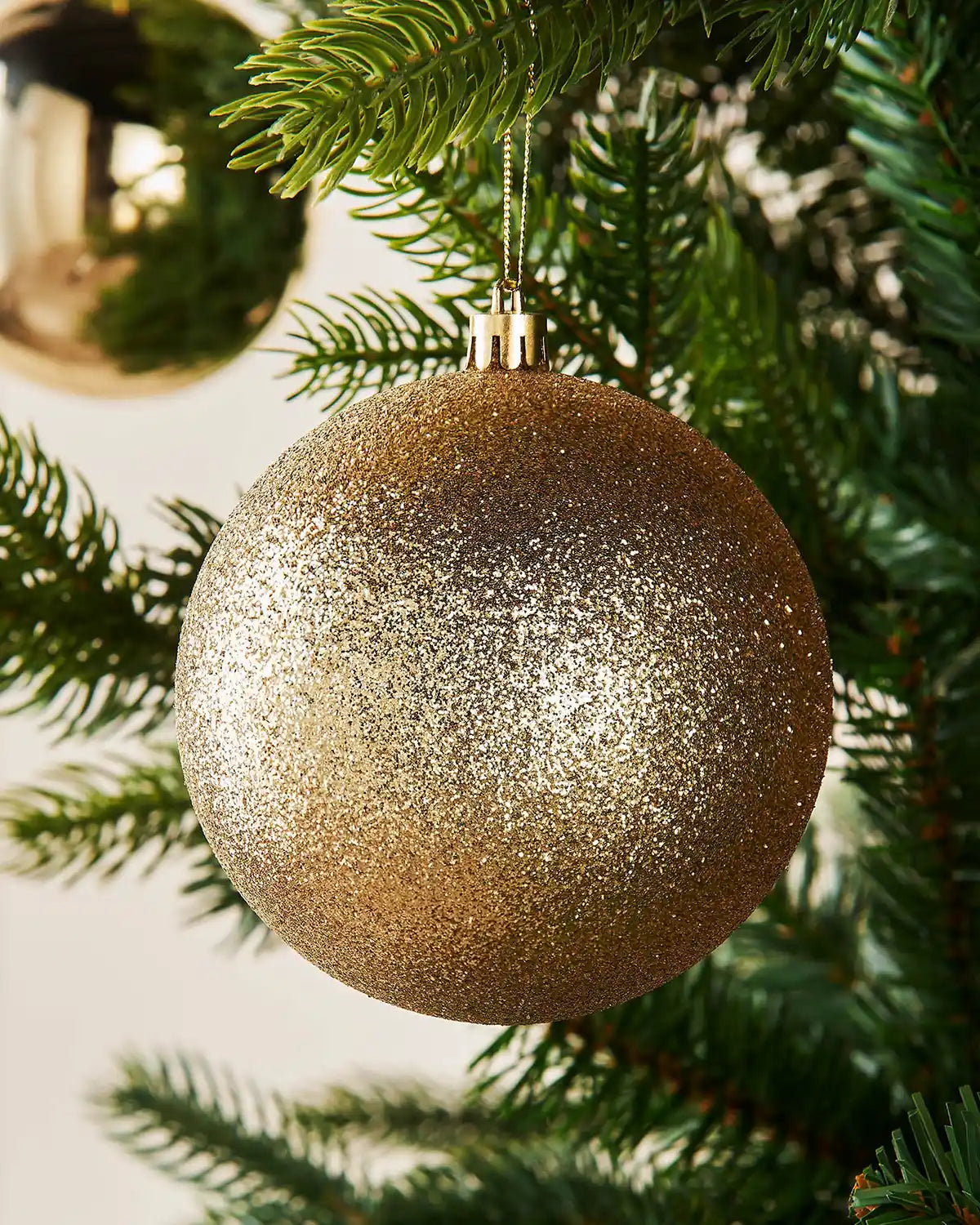 Gold glittery Christmas bauble hanging on a tree branch