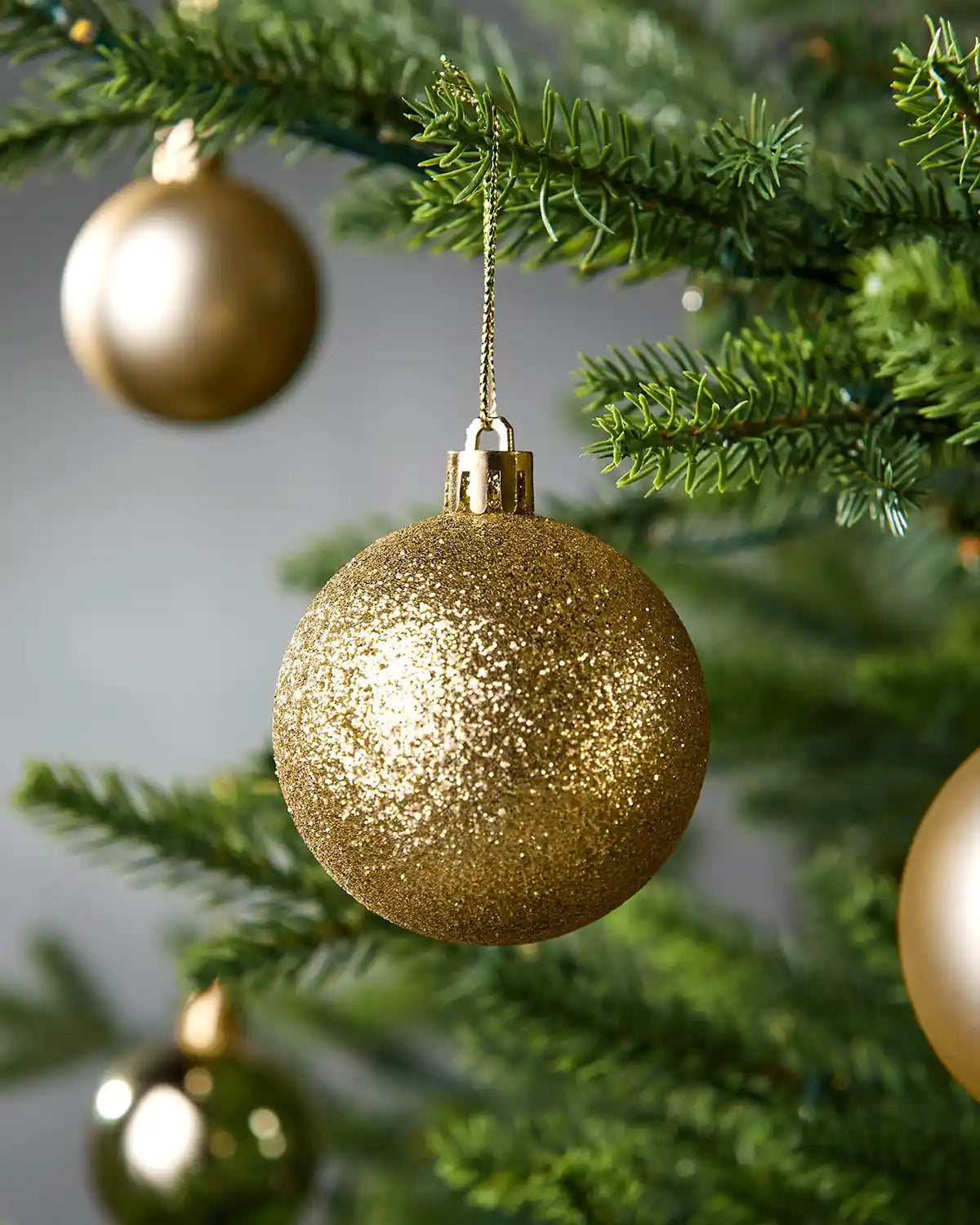 Gold glittery Christmas bauble hanging on a tree branch with a blurred background
