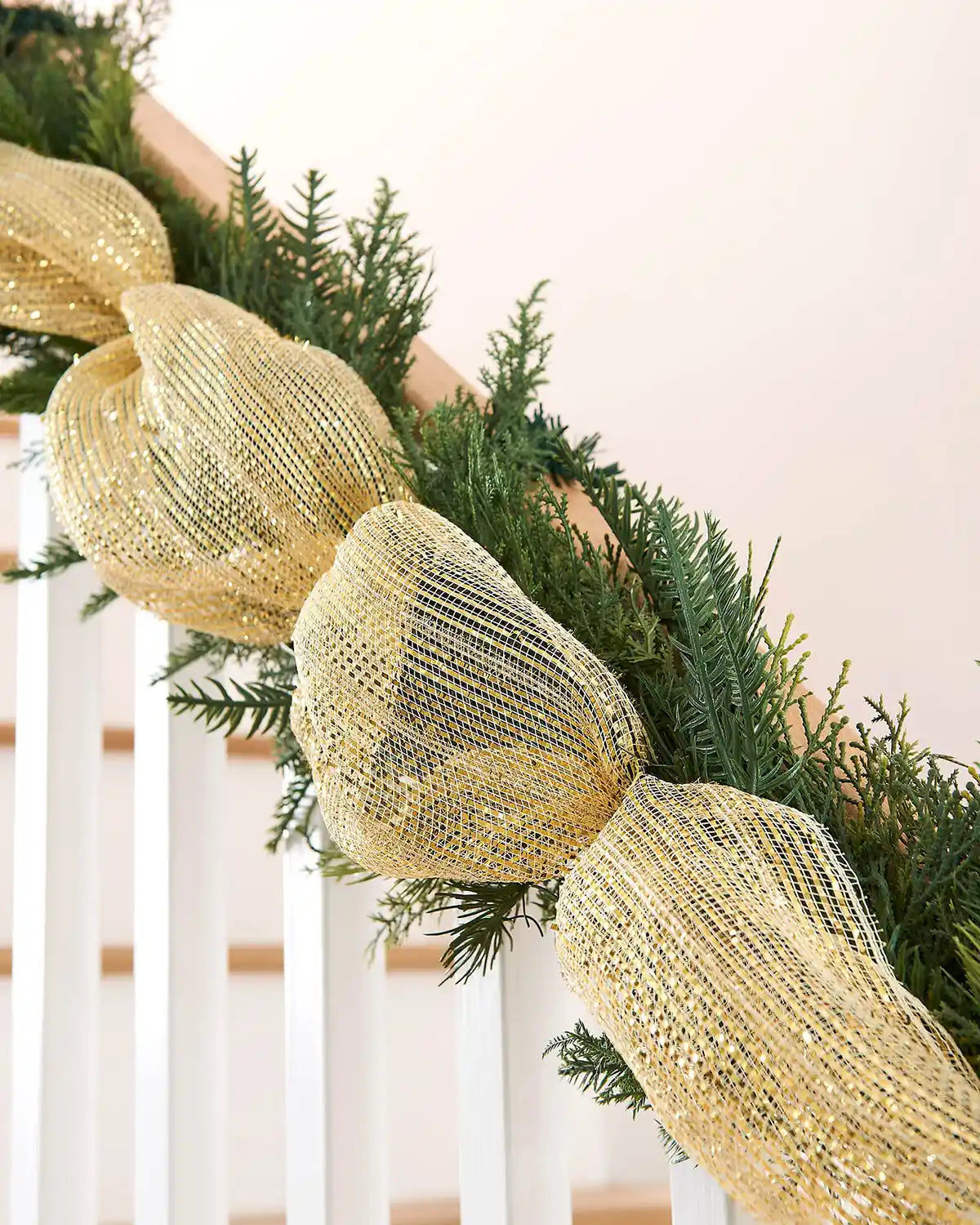 Gold mesh ribbon on a Christmas garland with a white staircase banister against a cream wall