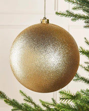 Gold oversized glitter bauble on a Christmas tree branch against a cream panel wall
