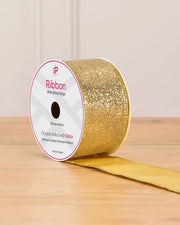 Gold sequin double sided wire edge ribbon in a cardboard roll on a wooden table against a light background