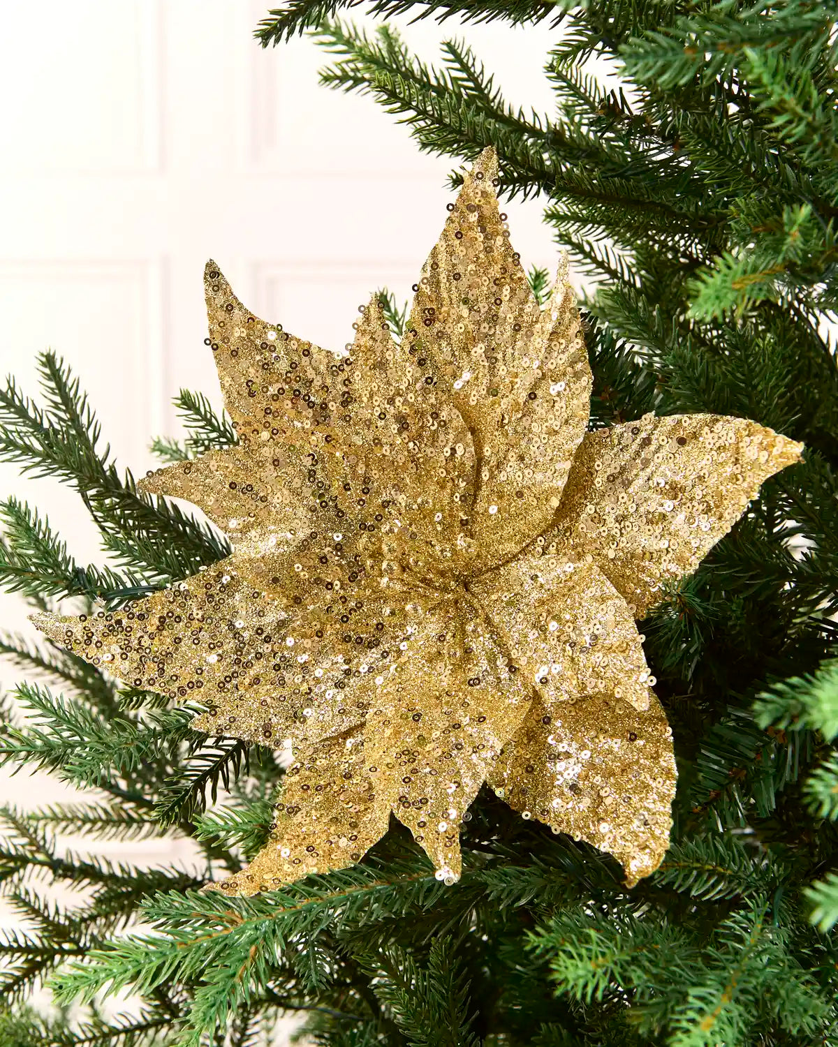 Gold sequin poinsettia flower on a Christmas tree against a light background 
