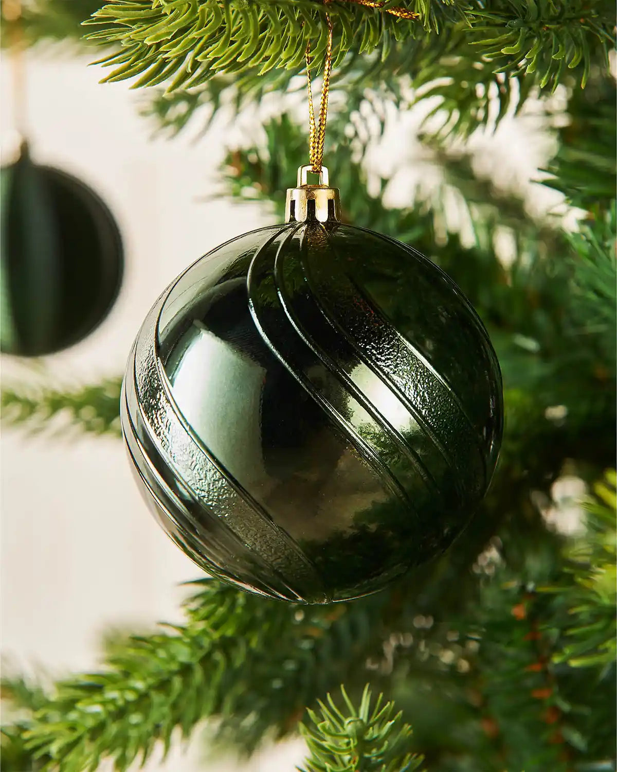 Green Christmas bauble on a tree branch with a blurry background