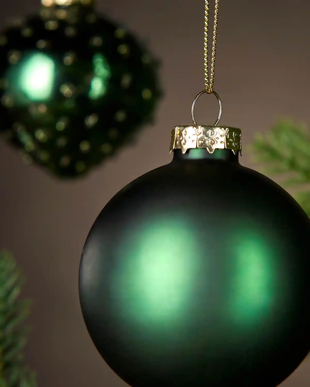 Green Christmas bauble with gold cap on a dark background