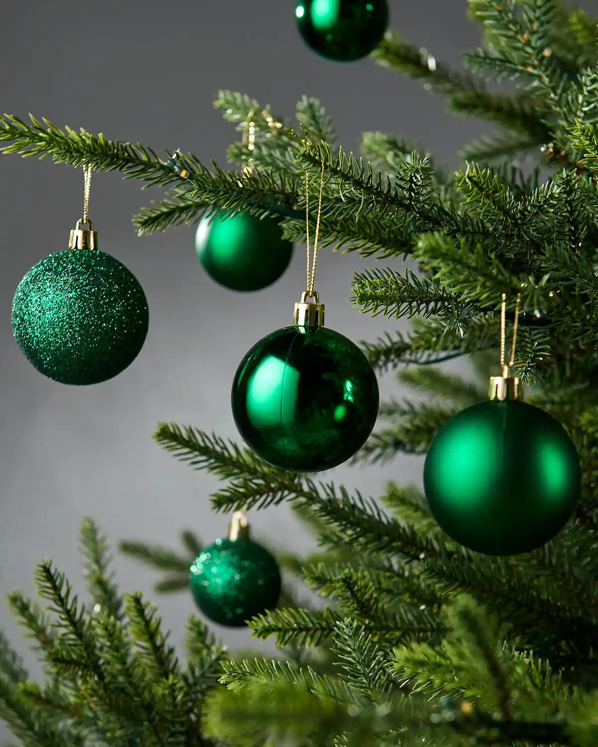 Green Christmas baubles on a tree against a grey background