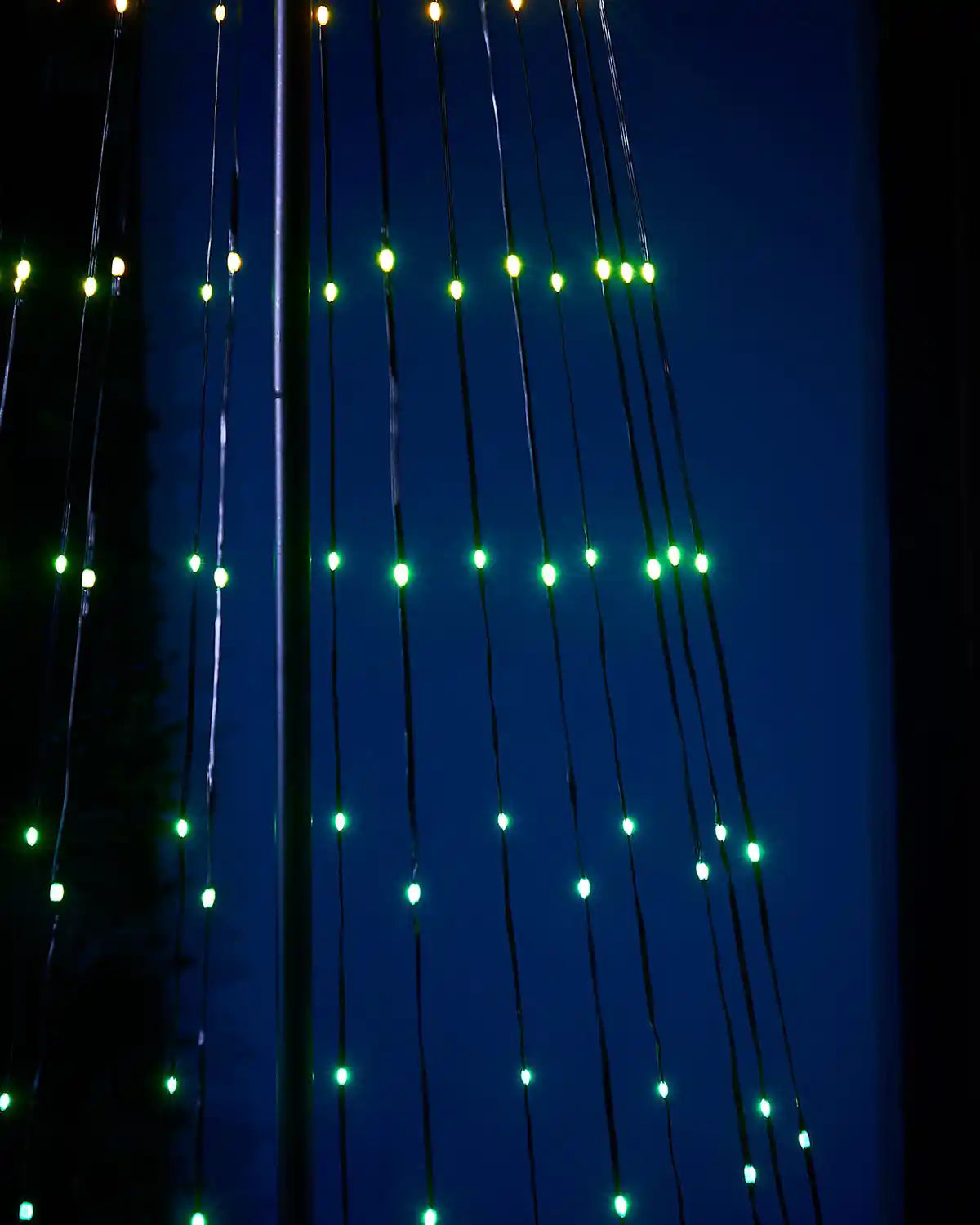 Green String lights in the shape of a tree hanging against a dark background
