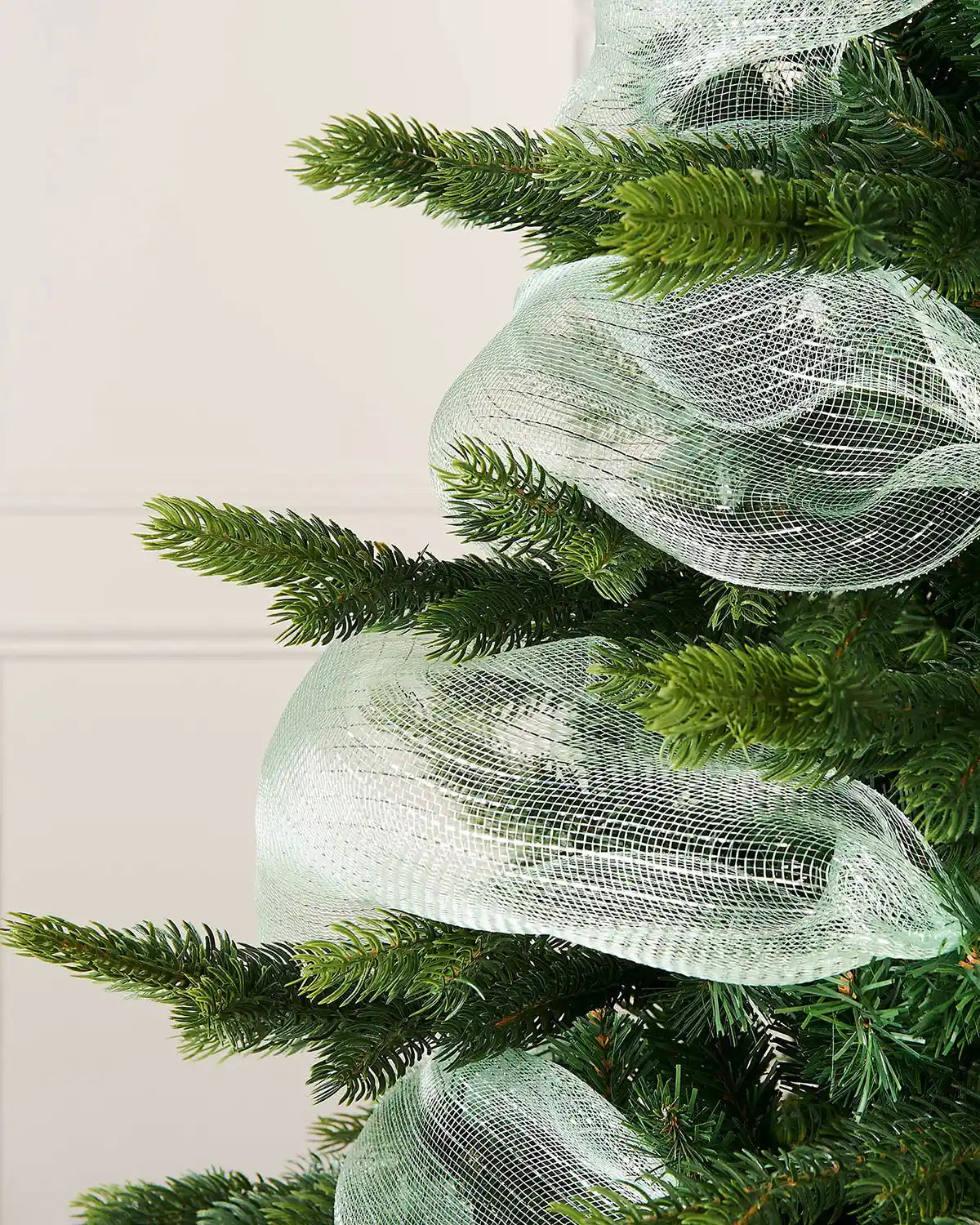 Green artificial Christmas tree with Mint green mesh ribbon against a white wall