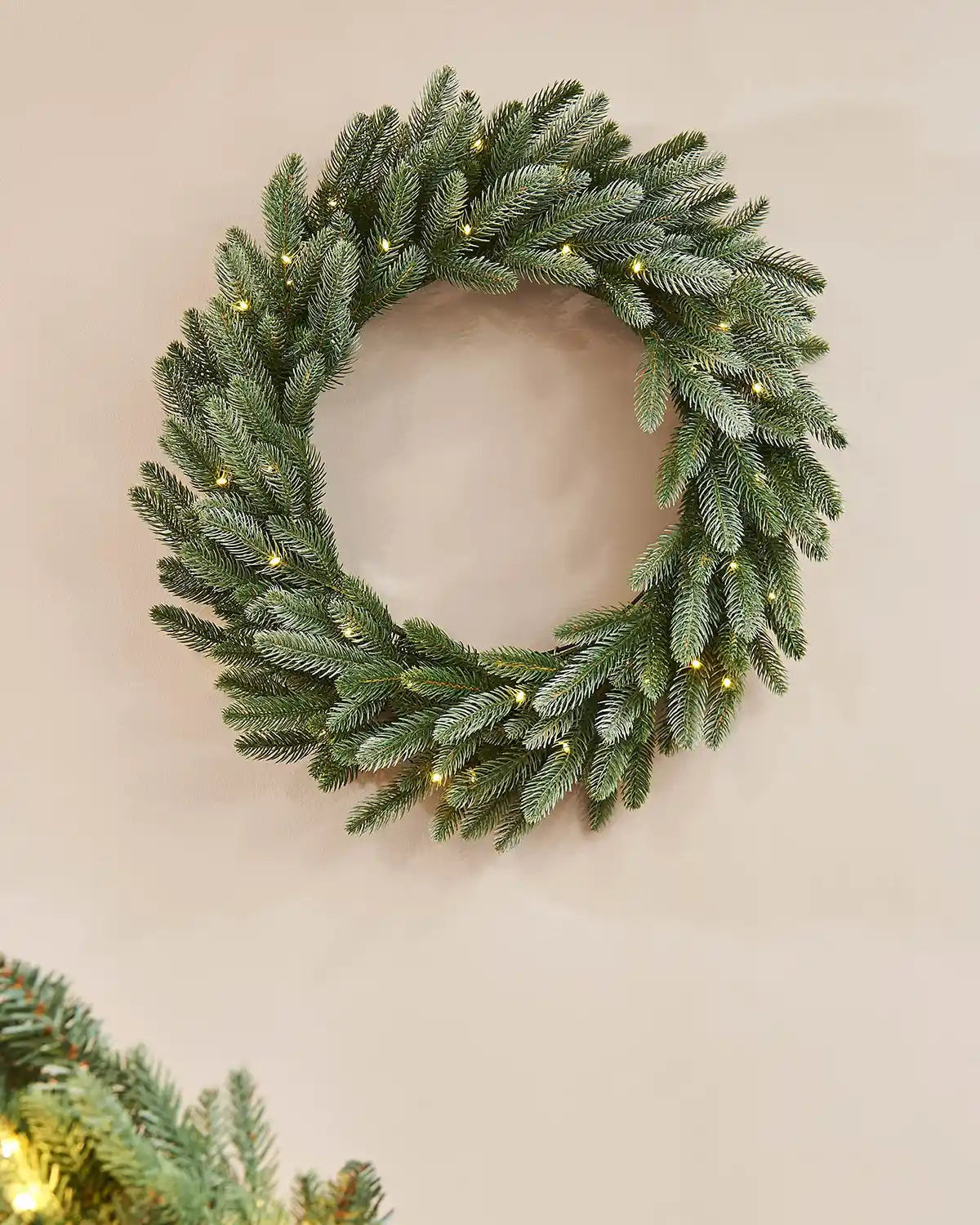 Green frosted Christmas wreath with warm white lights on a Beige wall
