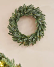 Green frosted Christmas wreath with warm white lights on a Beige wall