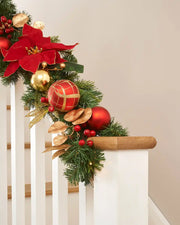 Green garland on wooden staircase featuring a combination of red and gold baubles, berries, and foliage